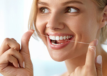 woman flossing her teeth for dental implant care in North Dallas