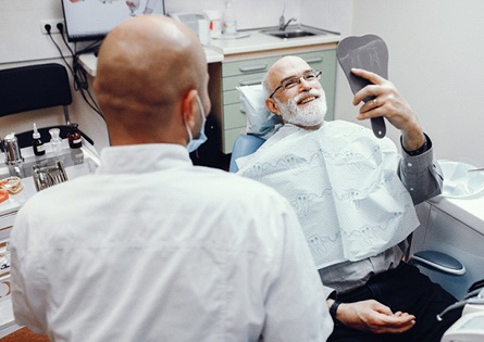 A male patient looking at his smile in the mirror after implant supported denture placement