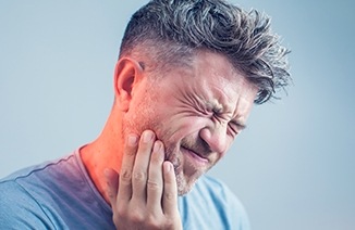 Man holding cheek in pain in need of restorative dentistry