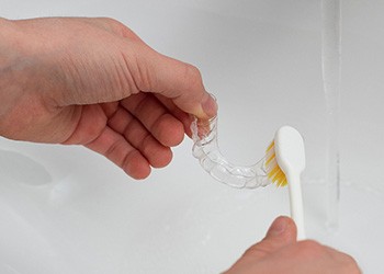 Patient cleaning clear aligner in sink