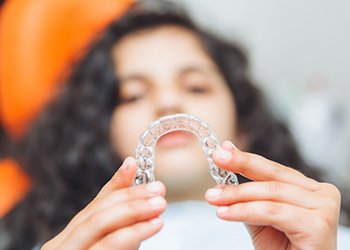 Teenage girl smiling while holding aligner in treatment chair