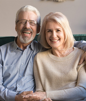 Senior couple smiling on their couch with All on 4 dental implants in North Dallas