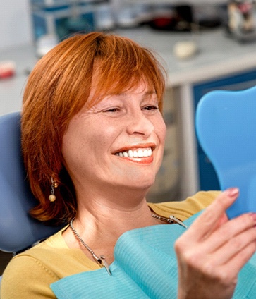 An older woman sitting in the dentist’s chair and looking in the mirror at her smile after using her Cigna dental insurance to cover her visit