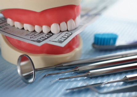 a jaw mockup biting a few hundred dollar bills next to some dental tools