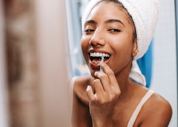 Woman using mirror to floss teeth