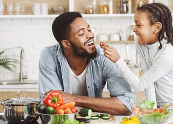 little kid giving their dad a cherry tomato in their kitchen