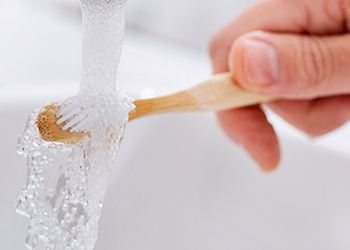 Rinsing off a wooden toothbrush in a porcelain sink