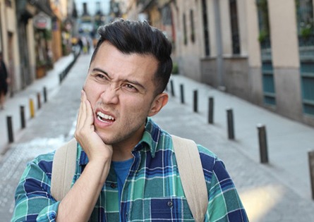 Grimacing man holding cheek before emergency dentistry