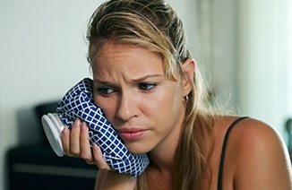 Woman holding ice pack to cheek in need of emergency dentistry