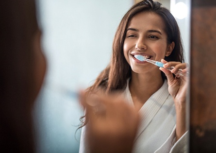 Woman smiling in mirror while brushing her teeth