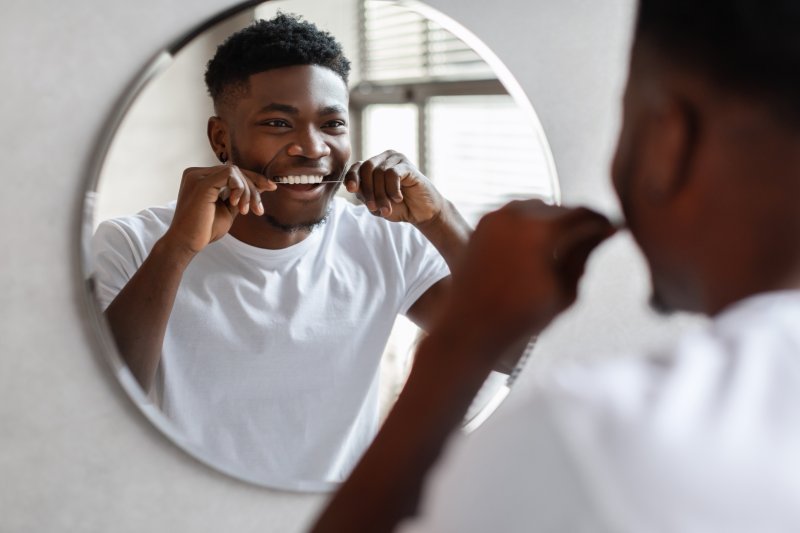 A man flossing between his teeth for proper dental implant care