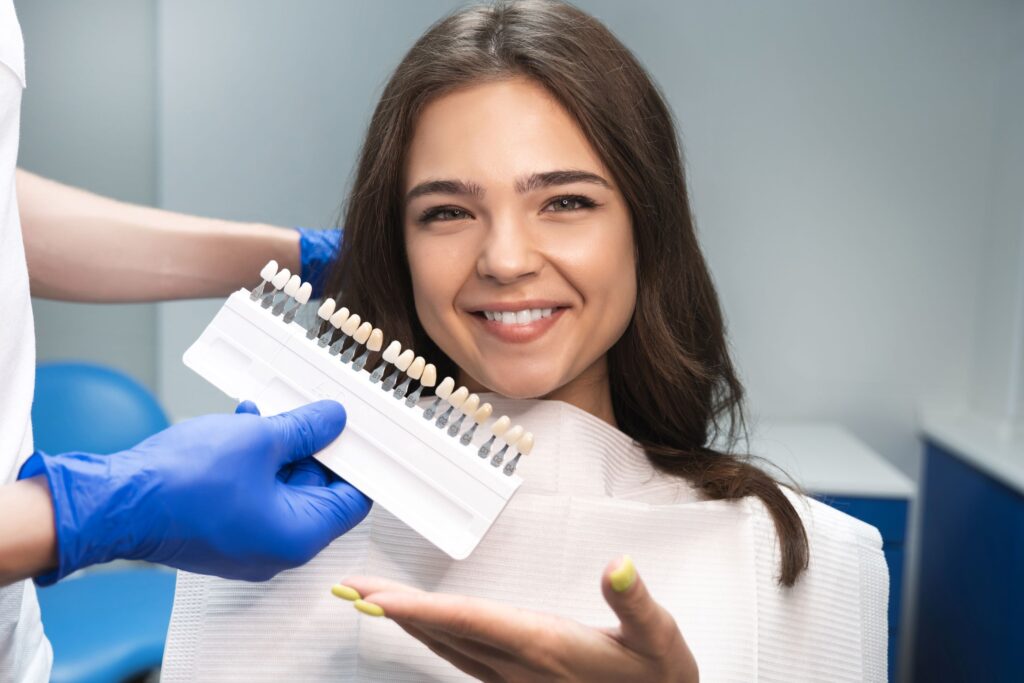 Woman smiling and gesturing to shade guide held to teeth